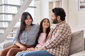 Happy indian family couple with teen child daughter bonding hugging talking sitting on couch at